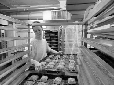 <span style='font-size:0.75em'><strong>Arbeit am Ofen</strong> Die Bäckerin holt ein Blech mit Brötchen aus dem Bäckereiwagen. Es kommt in den Ofen. ©Ernst Wilhelm Grüter</span>