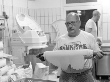 <span style='font-size:0.75em'><strong>Bäckerkuchen</strong> Der Bäcker bringt den ausgerollten Mürbeteig in den Nebenraum für die Kuchenherstellung. ©Ernst Wilhelm Grüter</span>