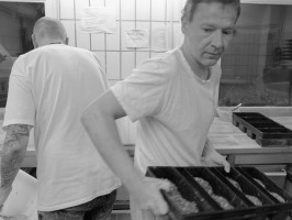 <span style='font-size:1.10em'>Die Brotteiglinge sind bereits in einer Kastenform. Der Bäcker ist kurz davor, die Form in einen Bäckereiwagen zu schieben.</span>