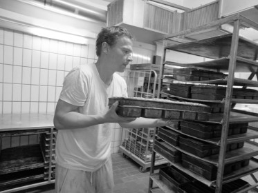 <span style='font-size:0.75em'><strong>Arbeit mit Teig</strong> Der Bäcker schiebt die Mehrfachform für Kasternbrote in den Bäckereiwagen. ©Ernst Wilhelm Grüter</span>