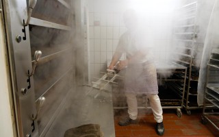 <span style='font-size:1.10em'>Ein Bäcker steht im Dampf einer gerade geschlossenen Ofenklappe.</span>