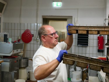 <span style='font-size:0.75em'><strong>Arbeiten mit Schablonen für Brotteig</strong> Die Brotteiglinge sind bereits in einer Kastenform. Der Bäcker ist kurz davor, die Form in einen Bäckereiwagen zu schieben. ©Ernst Wilhelm Grüter</span>