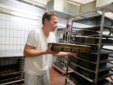 <span style='font-size:0.75em'><strong>Arbeiten mit Schablonen für Brotteig</strong> Der Bäcker schiebt die Mehrfachform für Kasternbrote in den Bäckereiwagen. ©Ernst Wilhelm Grüter</span>