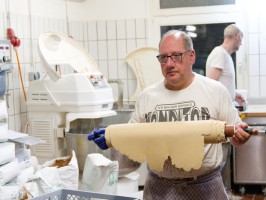 <span style='font-size:1.10em'>Ein Rolle Mürbeteig wird in den Nebenraum für das Backen eines Kuchens gebracht.</span>