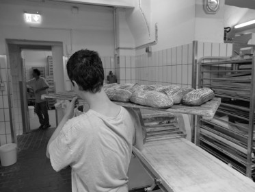 <span style='font-size:0.75em'><strong>Reportage Lindenbackt</strong> Ein Regalbrett mit Brotlaiben wird in das Ladengeschäft gebracht. Es liegt überm Hof. ©Ernst Wilhelm Grüter</span>